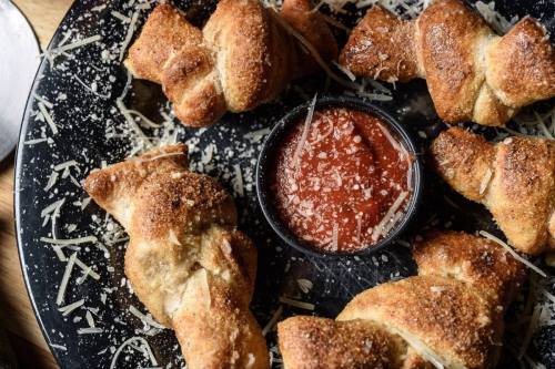 A plate of golden-brown bread knots sprinkled with cheese, served with a small bowl of marinara sauce.