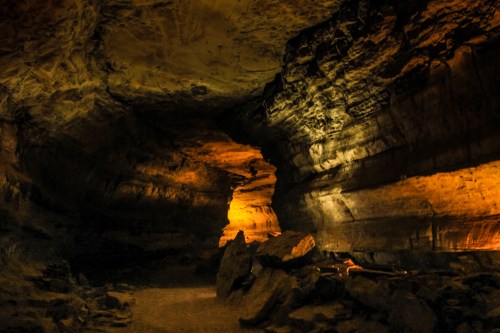 A dimly lit cave with textured rock formations and an illuminated column, creating a mysterious atmosphere.