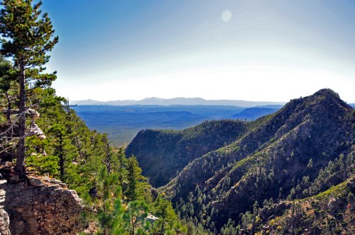 A panoramic view of rugged mountains and lush green trees under a clear blue sky.
