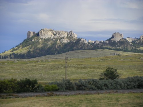 Rocky outcrop on a grassy hillside under a cloudy sky, with power lines in the foreground.