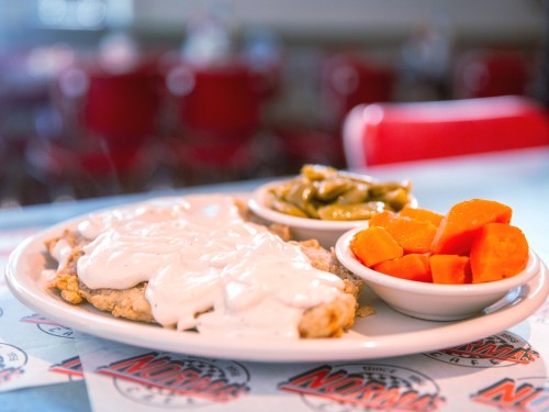 A plate of chicken fried steak topped with white gravy, served with green beans and diced carrots on the side.