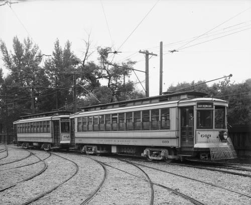 Two vintage streetcars on tracks, labeled "609" and "Saint Germain Co," surrounded by trees and utility poles.