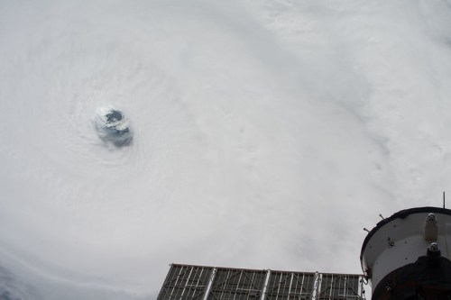 Aerial view of a hurricane's eye, with swirling clouds and part of a spacecraft in the foreground.