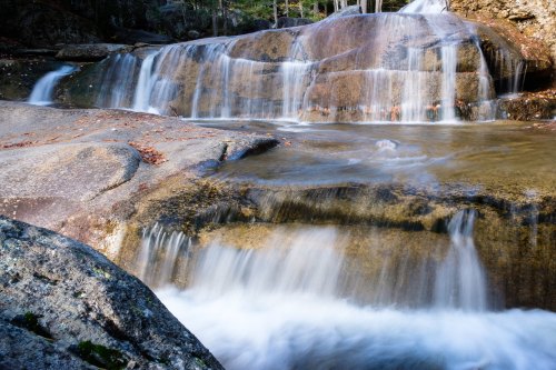 A serene waterfall cascading over smooth rocks, surrounded by lush greenery and gentle flowing water.