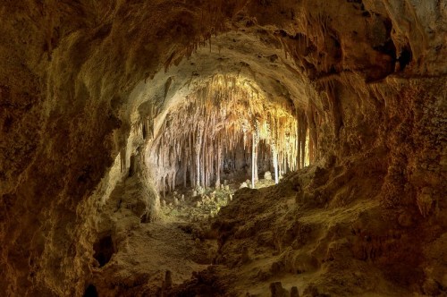 A dimly lit cave with stalactites hanging from the ceiling and rocky formations illuminated by soft light.