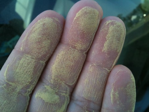 A close-up of a hand with yellow powder covering the fingertips and palm, resting on a reflective surface.