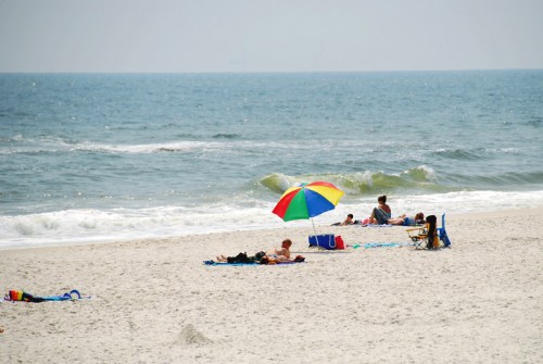 A sunny beach scene with people relaxing under a colorful umbrella, waves gently lapping at the shore.