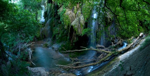A serene landscape featuring a lush green forest with cascading waterfalls and a tranquil stream.