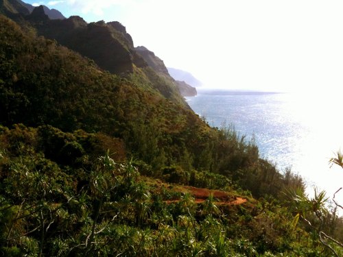 Scenic view of lush green mountains meeting a shimmering ocean under a bright sky.