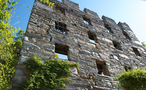 A weathered stone building with multiple windows, partially covered in greenery, set against a clear blue sky.