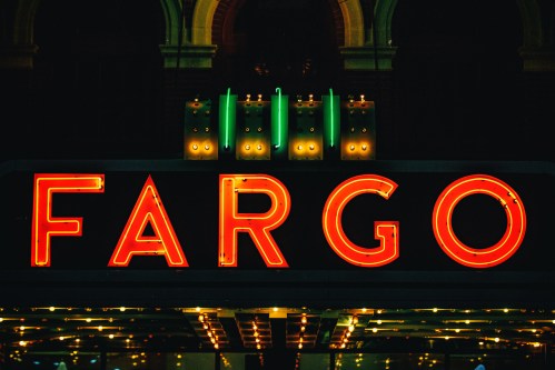 Neon sign reading "FARGO" illuminated at night, with decorative lights above and a vintage theater aesthetic.