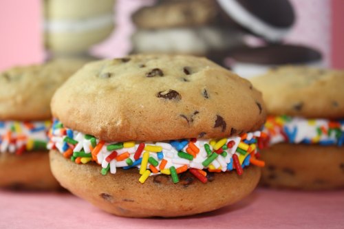 Close-up of cookie sandwiches filled with colorful sprinkles and cream, set against a pink background.