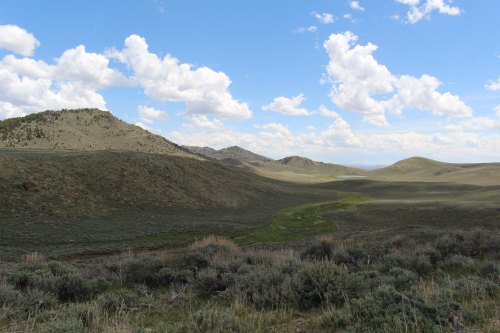 A scenic landscape featuring rolling hills, green valleys, and a blue sky with fluffy clouds.