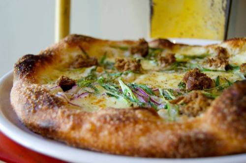 A close-up of a pizza with a golden crust, topped with herbs, cheese, and small pieces of meat.