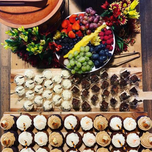 A colorful spread of desserts and fruits, including cupcakes, chocolate squares, and a variety of fresh berries and grapes.