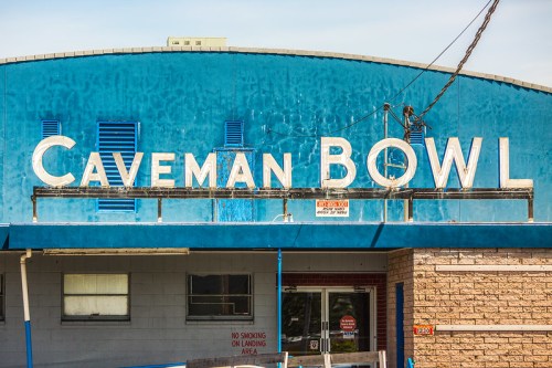 Sign for "Caveman Bowl" on a blue building, featuring large white letters and a clear sky in the background.