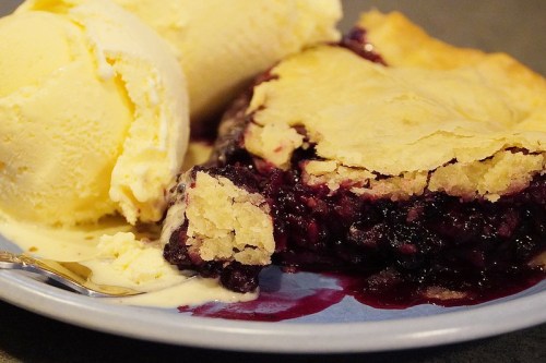 A slice of berry pie with a flaky crust, served alongside a scoop of vanilla ice cream on a blue plate.