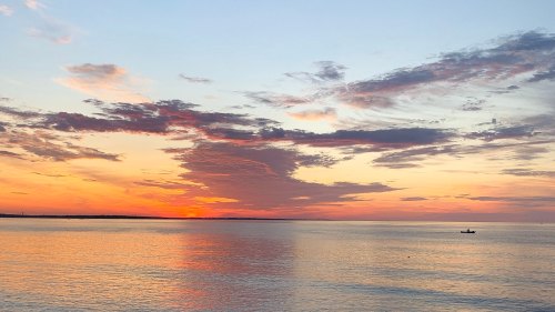 A serene sunset over calm waters, with vibrant orange and purple clouds reflecting on the surface.