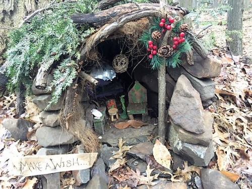 A small, whimsical fairy house made of stones and twigs, adorned with greenery and a sign that says "Make a Wish."