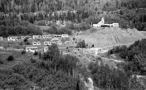 Black and white image of a mining town with houses on a hillside and a mine building in the background.