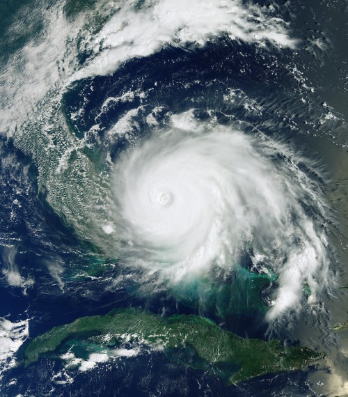 Satellite image of a powerful hurricane swirling over the ocean, with visible cloud formations and landmasses below.