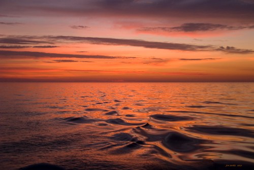A serene sunset over calm waters, with vibrant orange and purple hues reflecting on the surface.