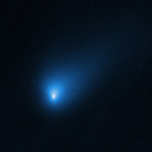 A bright blue comet with a glowing nucleus and a long, faint tail against a dark starry background.