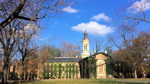 Historic building with a clock tower, surrounded by trees and blue sky, showcasing autumn foliage.
