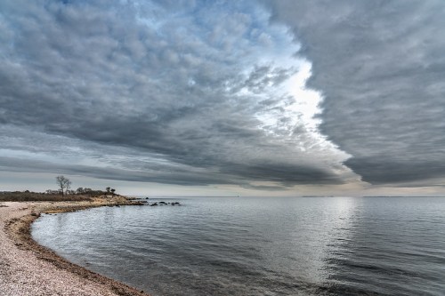 A tranquil shoreline with calm waters under a dramatic, cloudy sky.