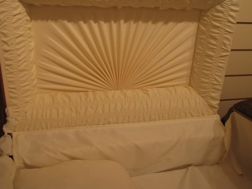A close-up of a decorative, pleated fabric headboard in soft cream tones, featuring intricate stitching and a smooth finish.