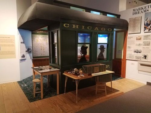 A museum exhibit featuring a replica of a Chicago train station with tables and historical displays.