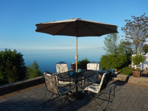 A patio table with chairs and an umbrella overlooking a calm lake and clear blue sky.