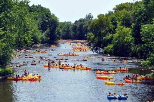 A busy river scene with many people floating on colorful inner tubes among trees and rocks.
