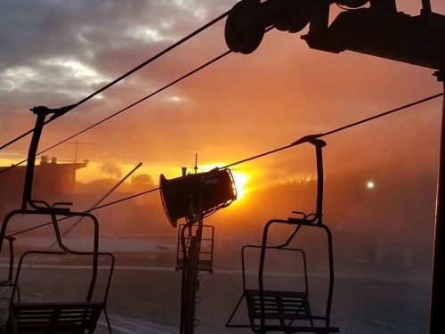 A ski lift silhouetted against a vibrant sunset, with mist rising in the foreground.