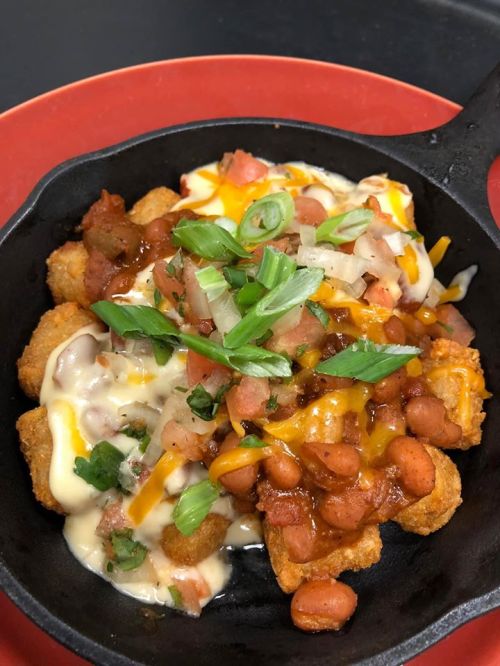 A skillet of loaded tater tots topped with cheese, beans, tomatoes, and green onions.