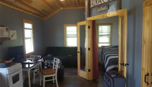 Cozy interior of a small cabin with a kitchen, dining area, and a bedroom, featuring wooden accents and natural light.