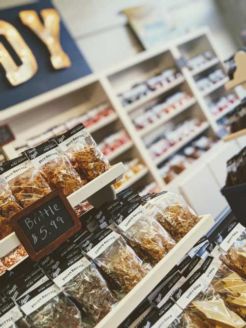 A display of various snack bags, including brittle, in a shop with shelves filled with colorful treats.