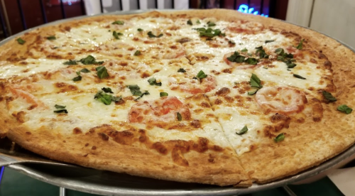 A freshly baked pizza with melted cheese, sliced tomatoes, and fresh basil on a metal serving tray.