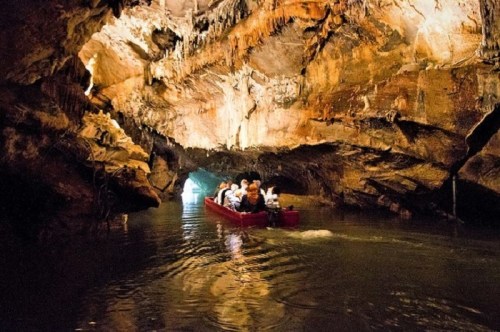 A group of people in a small boat navigating through a dark cave with stalactites and water reflections.