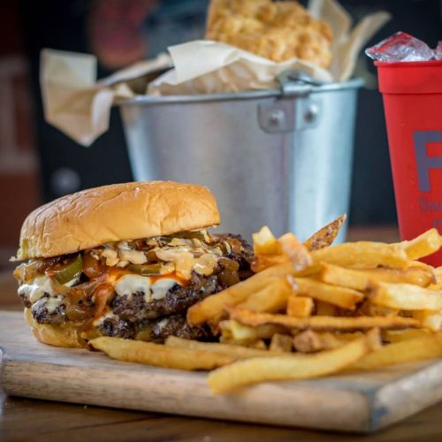 A juicy burger topped with melted cheese and toppings, served with crispy fries and a drink in a red cup.