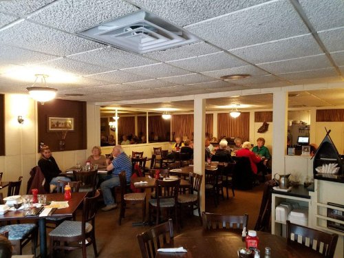 A cozy restaurant interior with diners at tables, warm lighting, and a mirrored wall reflecting the atmosphere.