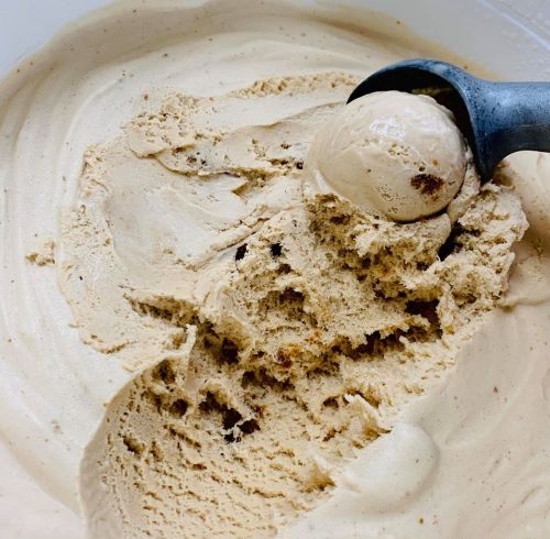 A close-up of creamy coffee ice cream with a scoop resting on top, showing a smooth, textured surface.