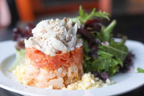 A layered seafood dish with shrimp and crab atop a bed of greens, served on a white plate.