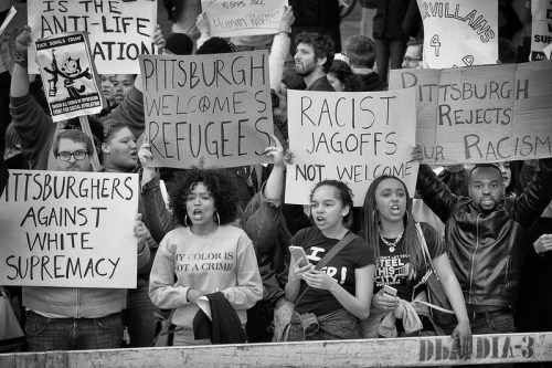 Black and white image of protesters holding signs against racism and in support of refugees in Pittsburgh.