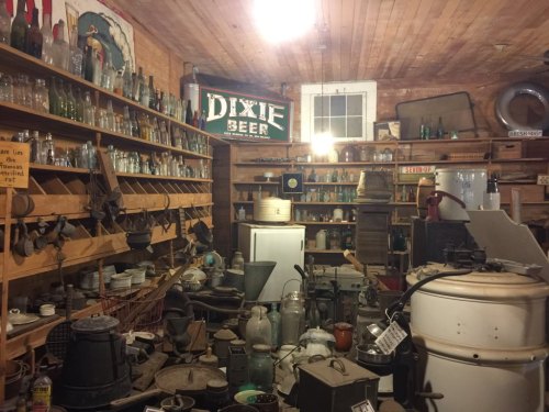 A cluttered vintage store filled with old bottles, kitchenware, and various antiques on wooden shelves.