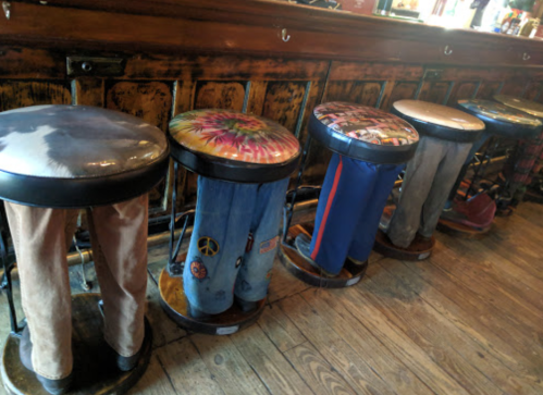 Colorful bar stools with unique seat designs and fabric-covered legs resembling pants, lined up at a wooden bar.