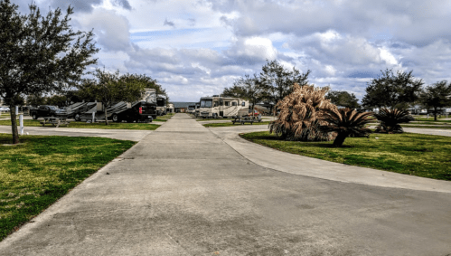 A paved pathway through a park with RVs, trees, and shrubs under a cloudy sky.