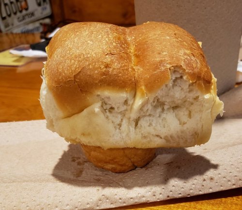 A partially eaten dinner roll resting on a napkin, with a soft texture and golden-brown crust.