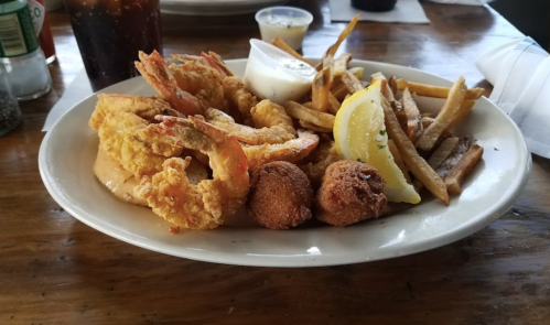A plate of fried shrimp, hushpuppies, fries, and a lemon wedge, served with a dipping sauce.