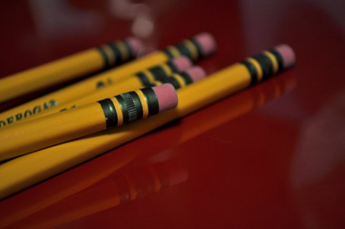 A close-up of yellow pencils with pink erasers, resting on a reflective red surface.